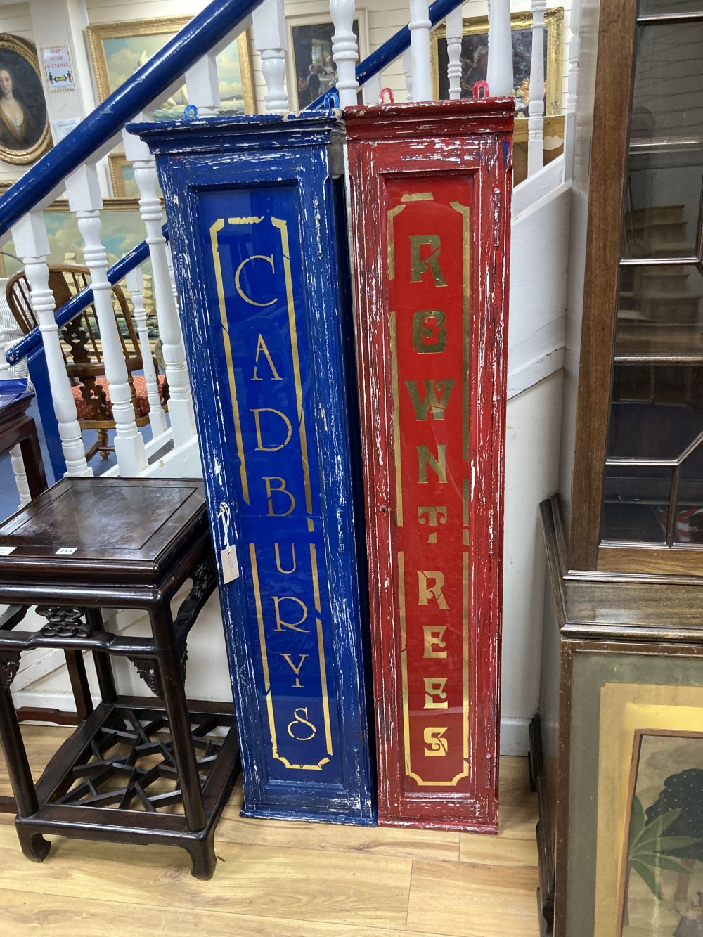 Two painted wood shop display cabinets, the glass doors marked Cadburys and Rowntrees, largest width 34cm height 140cm